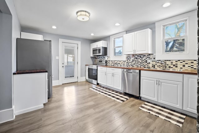 kitchen featuring decorative backsplash, stainless steel appliances, white cabinetry, wooden counters, and a sink