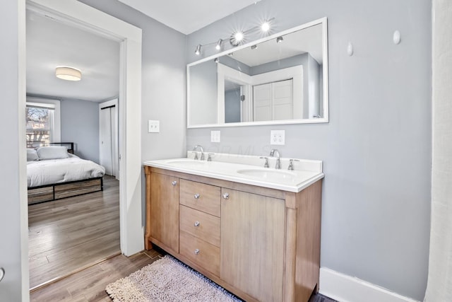 ensuite bathroom featuring double vanity, a sink, ensuite bath, and wood finished floors