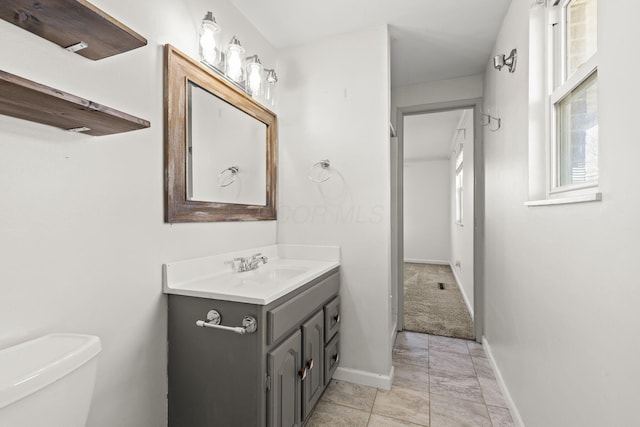 half bathroom with vanity, toilet, and baseboards