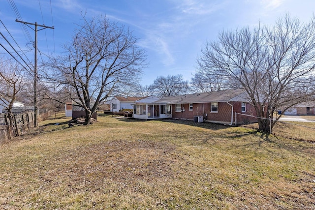 exterior space featuring central AC, brick siding, a front yard, and a sunroom