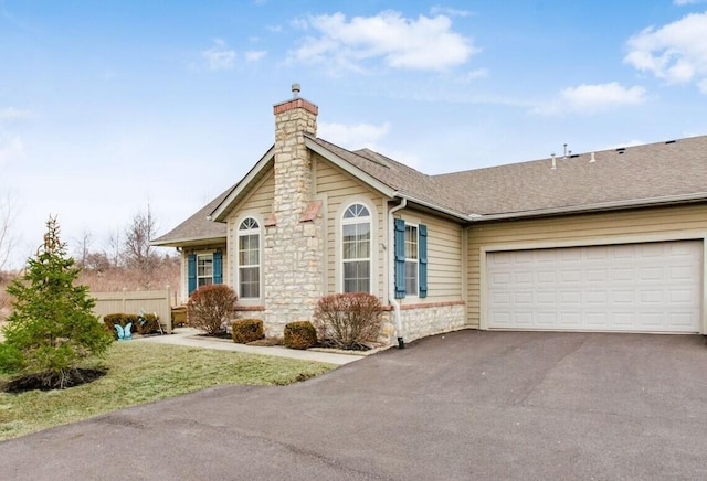 view of front facade with an attached garage, a shingled roof, driveway, stone siding, and a chimney