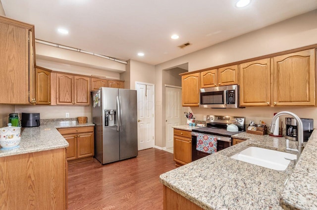 kitchen with visible vents, light stone countertops, stainless steel appliances, light wood-style floors, and a sink