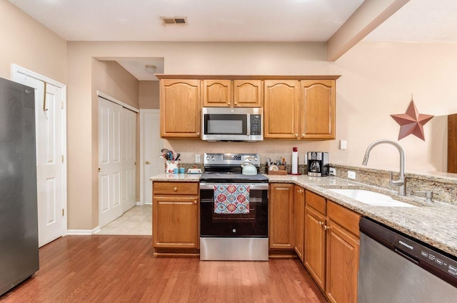 kitchen with light stone counters, appliances with stainless steel finishes, a sink, and visible vents