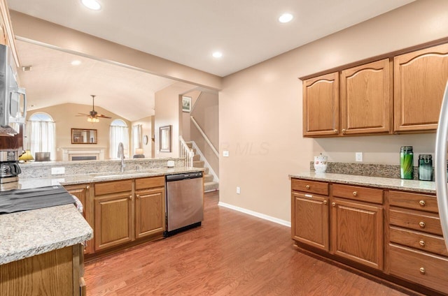 kitchen featuring a fireplace, a sink, vaulted ceiling, appliances with stainless steel finishes, and light wood finished floors