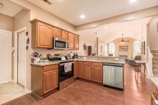 kitchen featuring lofted ceiling, stainless steel appliances, a peninsula, a fireplace, and a sink