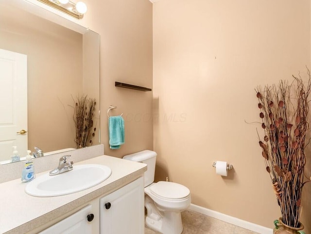 half bath with toilet, tile patterned floors, baseboards, and vanity