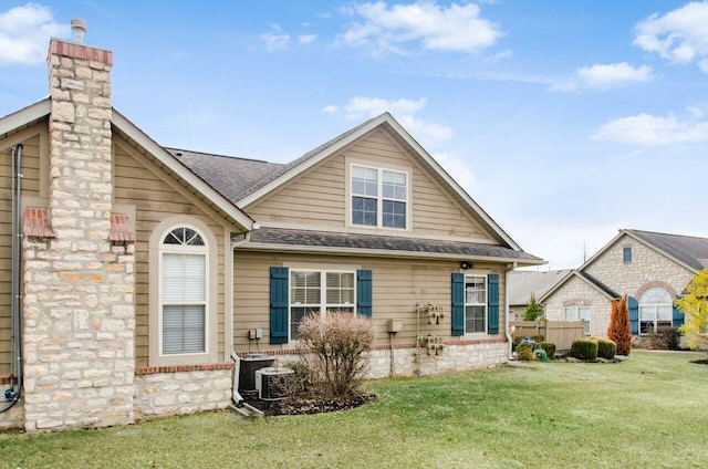 view of front of home with a front yard, roof with shingles, a chimney, and central air condition unit