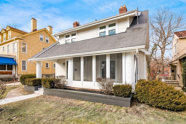 view of front of property with roof with shingles, a chimney, and a sunroom