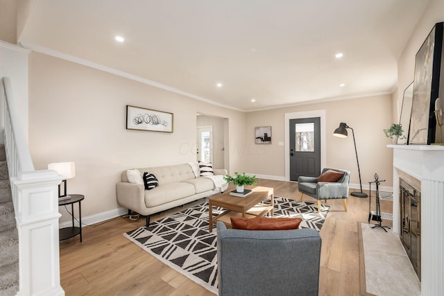 living room with a fireplace, light wood finished floors, ornamental molding, baseboards, and stairs