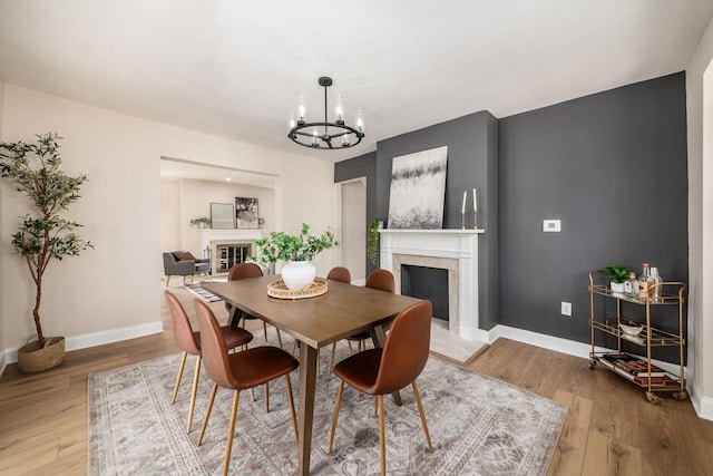 dining room with light wood-style floors, a high end fireplace, a notable chandelier, and baseboards