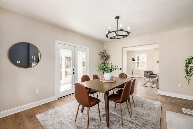 dining room featuring french doors, a notable chandelier, visible vents, wood finished floors, and baseboards