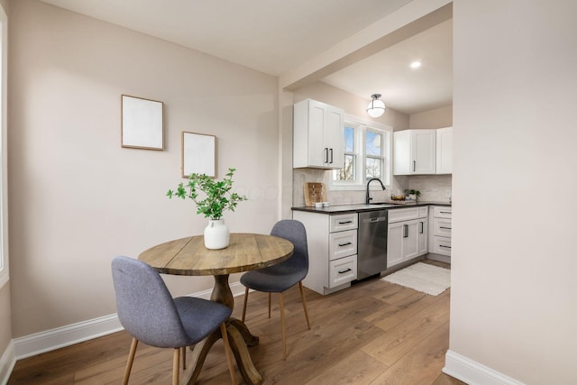 kitchen featuring dark countertops, backsplash, wood finished floors, dishwasher, and baseboards