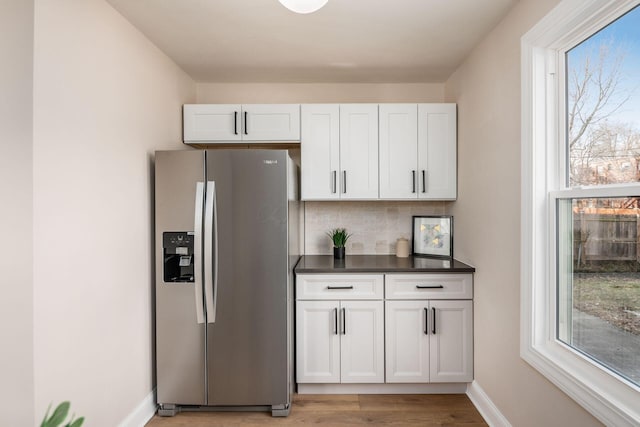 kitchen featuring stainless steel fridge, tasteful backsplash, baseboards, dark countertops, and light wood-style floors