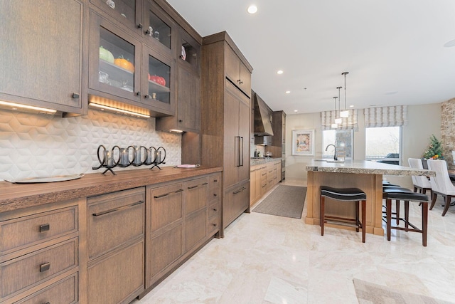 105 N Riverview St Unit 216, Dublin, OH 43017 - kitchen featuring tasteful backsplash, a sink, a kitchen breakfast bar, glass insert cabinets, and wall chimney exhaust hood