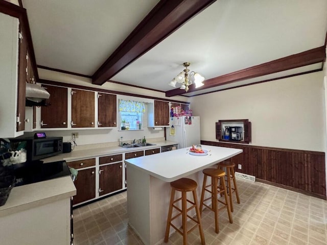 kitchen with a wainscoted wall, beamed ceiling, freestanding refrigerator, light countertops, and black microwave