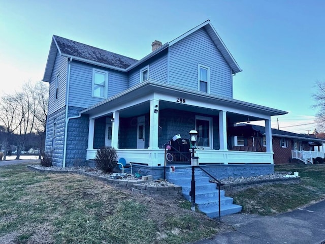 view of front of property with covered porch, a chimney, and a front yard