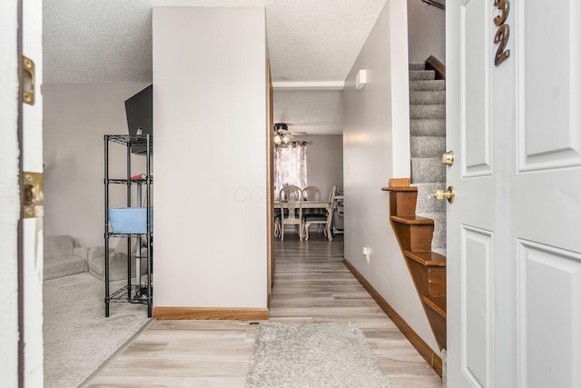 hall with baseboards, light wood-style flooring, stairway, and a textured ceiling