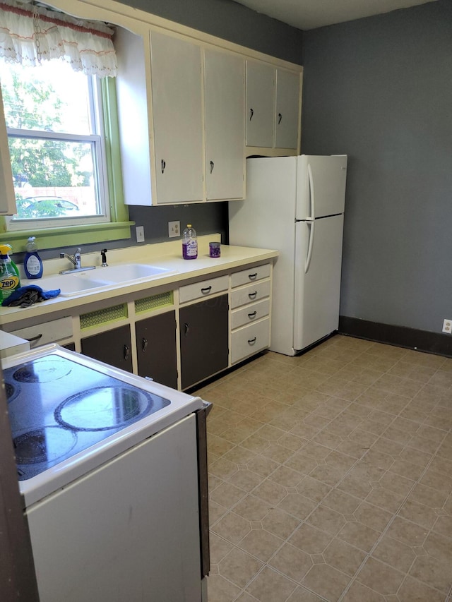 kitchen with baseboards, stove, freestanding refrigerator, light countertops, and a sink