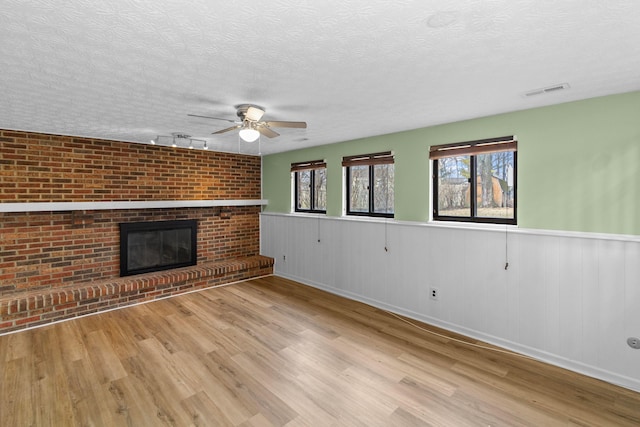 unfurnished living room featuring a brick fireplace, wainscoting, a textured ceiling, and wood finished floors