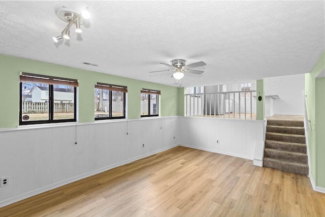 empty room with visible vents, wainscoting, stairway, wood finished floors, and a textured ceiling