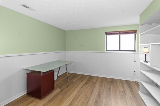 home office featuring wainscoting, visible vents, a textured ceiling, and wood finished floors