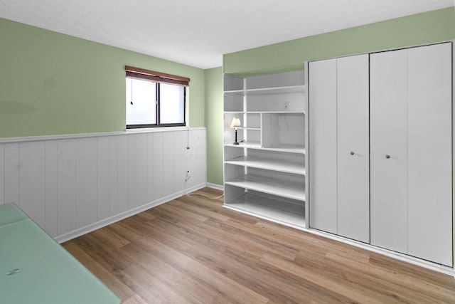 unfurnished bedroom featuring a wainscoted wall, a closet, and wood finished floors