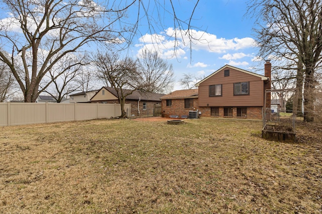 back of house featuring brick siding, a yard, a chimney, central AC unit, and fence