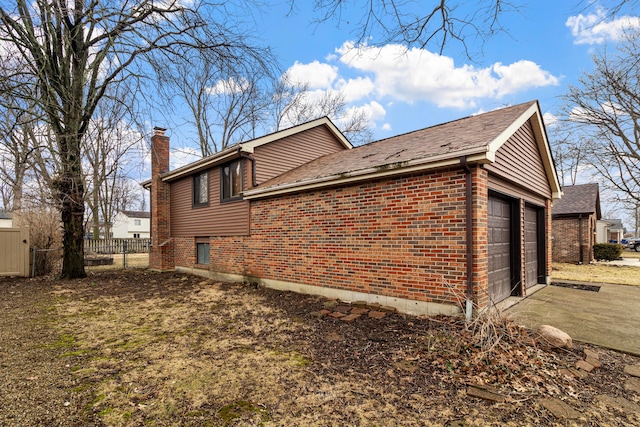 view of side of home with brick siding, fence, a chimney, and an attached garage