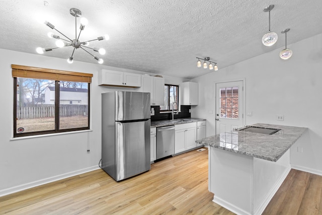 kitchen featuring a peninsula, vaulted ceiling, stainless steel appliances, light wood-type flooring, and a sink