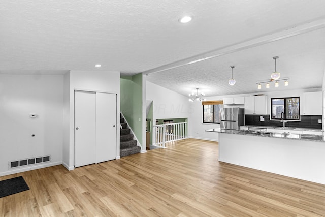 kitchen featuring visible vents, lofted ceiling, freestanding refrigerator, light wood-type flooring, and white cabinetry