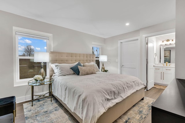 bedroom featuring light wood finished floors, multiple windows, baseboards, and ensuite bathroom