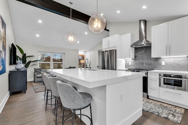 kitchen featuring lofted ceiling with beams, stainless steel appliances, a sink, backsplash, and wall chimney exhaust hood