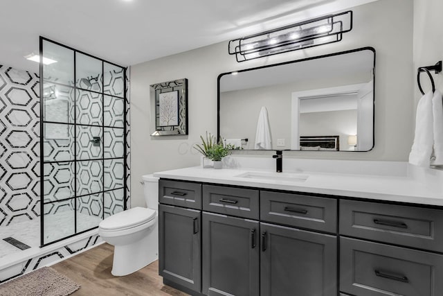 bathroom with toilet, wood finished floors, a tile shower, and vanity