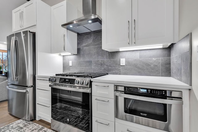 kitchen featuring white cabinetry, appliances with stainless steel finishes, light wood-type flooring, backsplash, and wall chimney exhaust hood