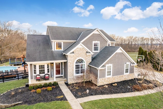 traditional-style home with a shingled roof, stone siding, fence, and stucco siding