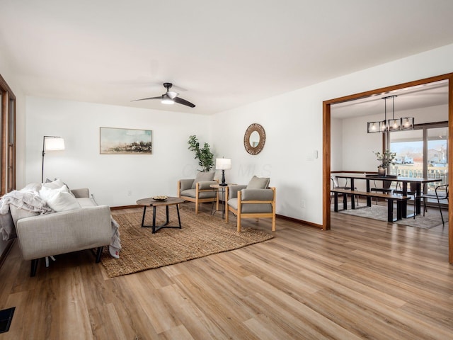 living area with ceiling fan with notable chandelier, baseboards, and light wood-style floors