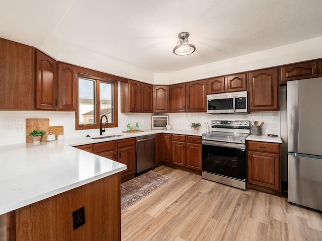 kitchen with a sink, light countertops, appliances with stainless steel finishes, light wood-type flooring, and decorative backsplash