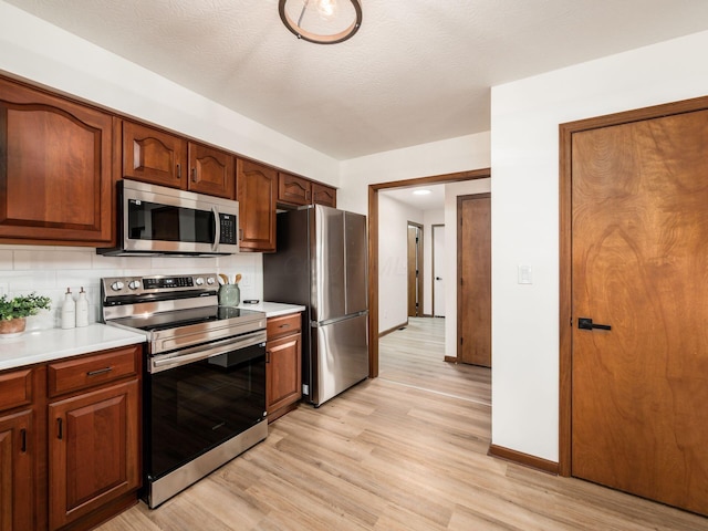 kitchen featuring light wood-style flooring, stainless steel appliances, baseboards, light countertops, and backsplash