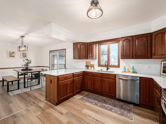 kitchen featuring light countertops, appliances with stainless steel finishes, light wood-style floors, a sink, and a peninsula