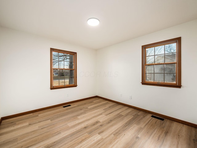 empty room with light wood-type flooring, baseboards, visible vents, and a wealth of natural light