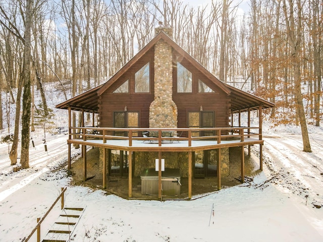 snow covered property with stone siding, a chimney, log exterior, and a wooden deck