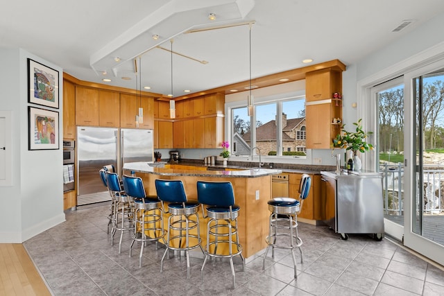 kitchen featuring visible vents, dark stone counters, built in fridge, a kitchen breakfast bar, and a center island