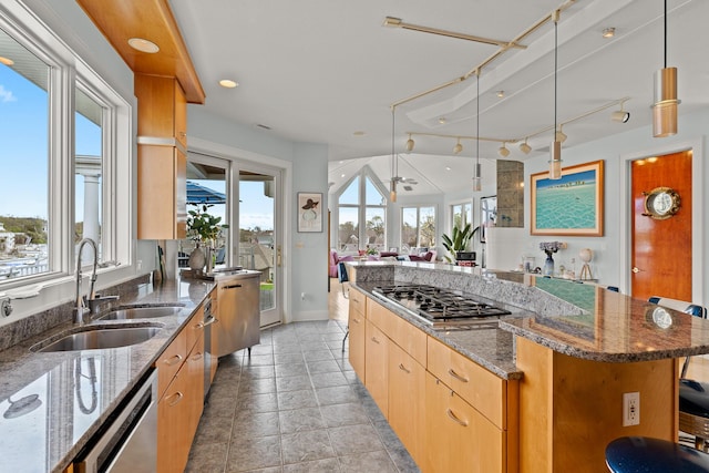 kitchen featuring dark stone countertops, stainless steel appliances, a sink, open floor plan, and a center island