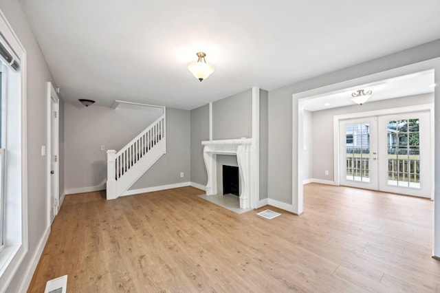 unfurnished living room featuring stairs, french doors, light wood-type flooring, and visible vents