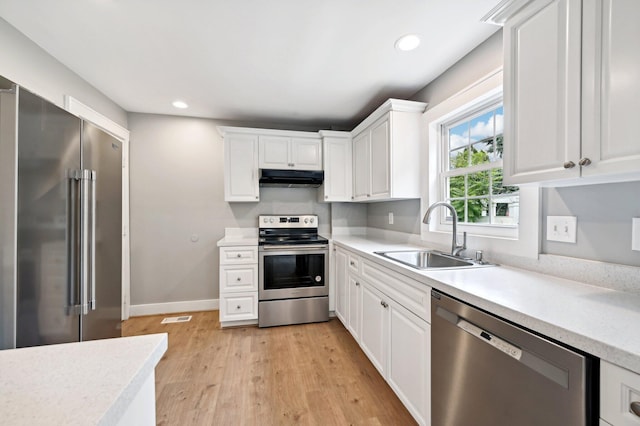 kitchen featuring white cabinets, appliances with stainless steel finishes, light countertops, under cabinet range hood, and a sink