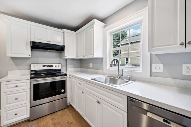 kitchen featuring under cabinet range hood, a sink, white cabinets, light countertops, and appliances with stainless steel finishes