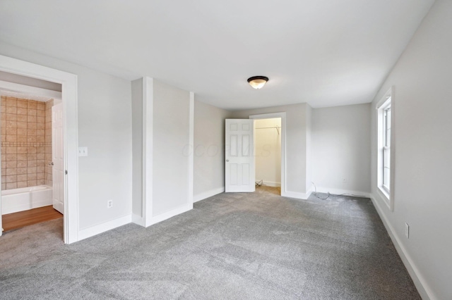 unfurnished bedroom with carpet floors, connected bathroom, a spacious closet, and baseboards