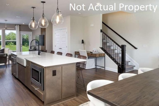 kitchen featuring dark wood-type flooring, stainless steel microwave, a breakfast bar area, and an island with sink