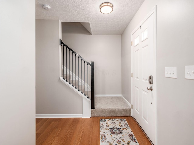 entrance foyer featuring baseboards, a textured ceiling, wood finished floors, and stairs