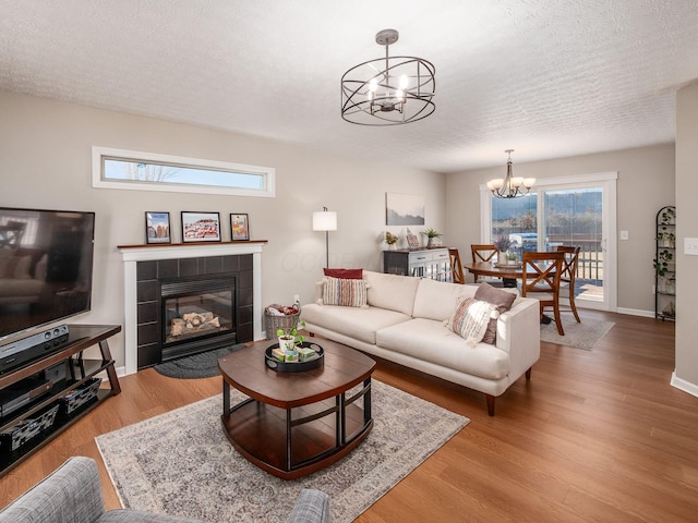 living area featuring baseboards, a chandelier, a tiled fireplace, wood finished floors, and a textured ceiling